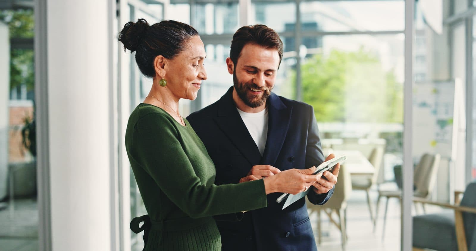 Duas pessoas de equipe corporativa conversando e consultando um tablet em ambiente de escritório