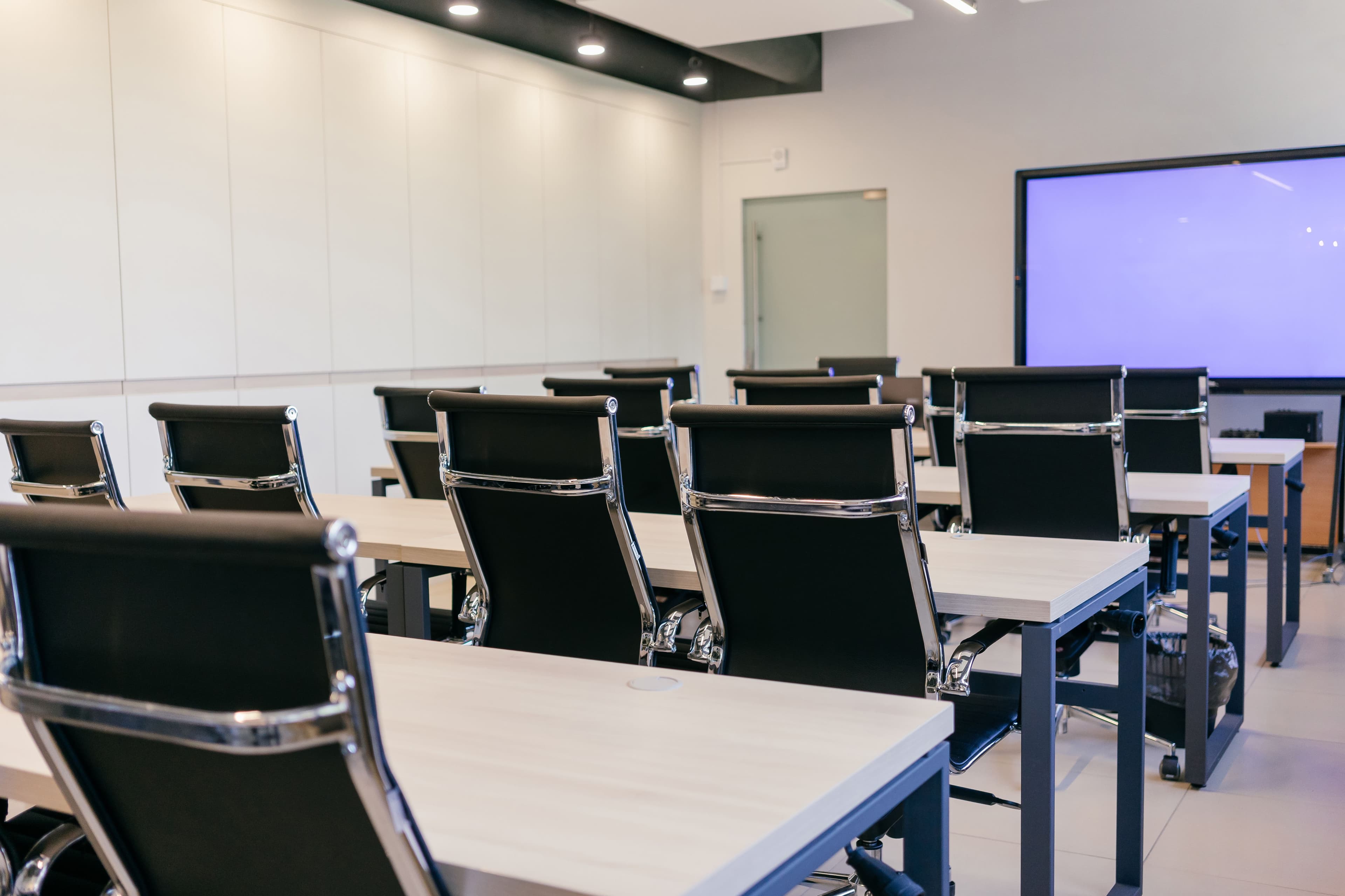 Sala de treinamento com fileiras de mesas, cadeiras e telão